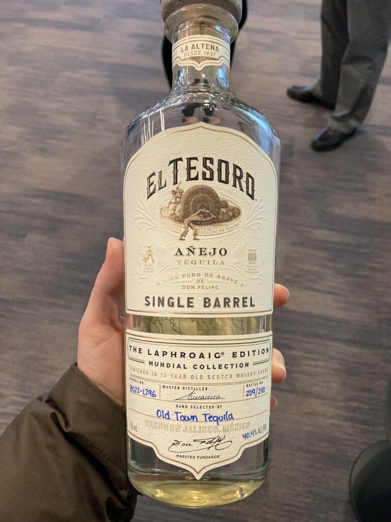 A hand holding a bottle of El Tesoro's Mundial Collection Añejo Tequila, a collaboration with Laphroaig Distillery. 