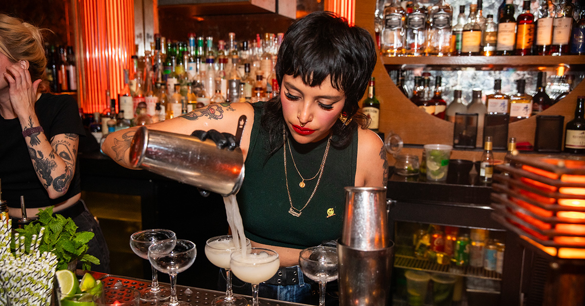 Striking bartender at Part Time Lover in San Diego skillfully pouring cocktails from a mixer into a row of coupe glasses during 2024 Bartender's Weekend. The trendy venue features vinyl records and craft cocktails in a laid-back atmosphere where RBS certification is required for alcohol service.